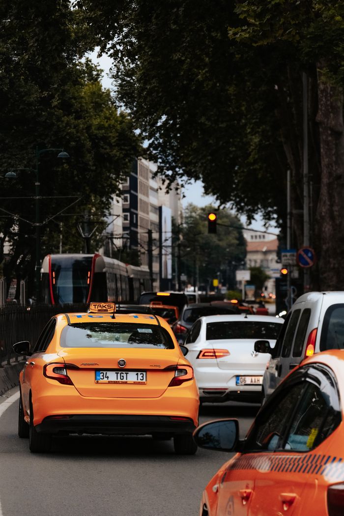 services-01 A bustling street scene featuring a yellow taxi amid city traffic under large trees.