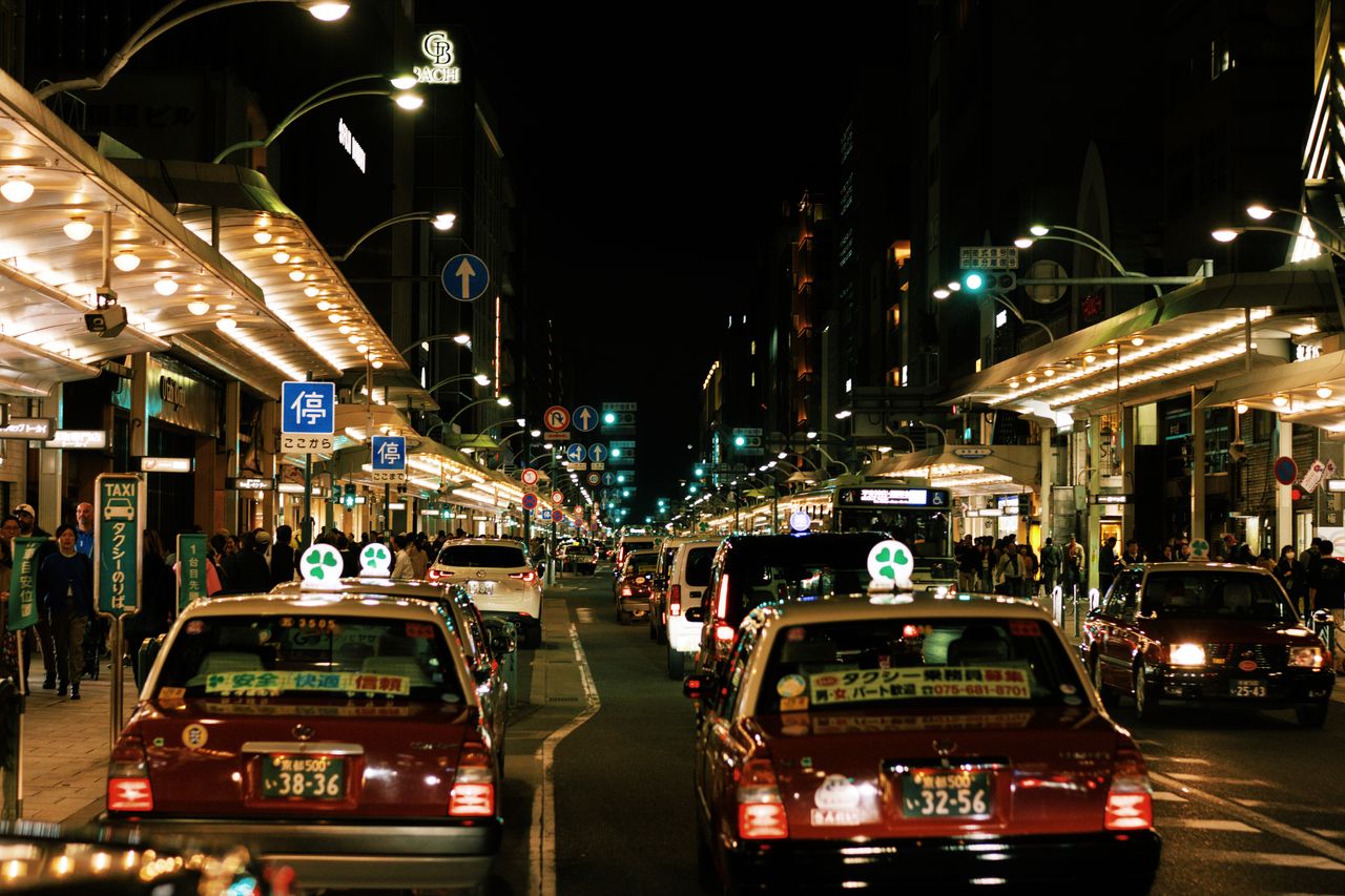 services-03 Vibrant night scene in Kyoto featuring busy streets and iconic Japanese taxis.