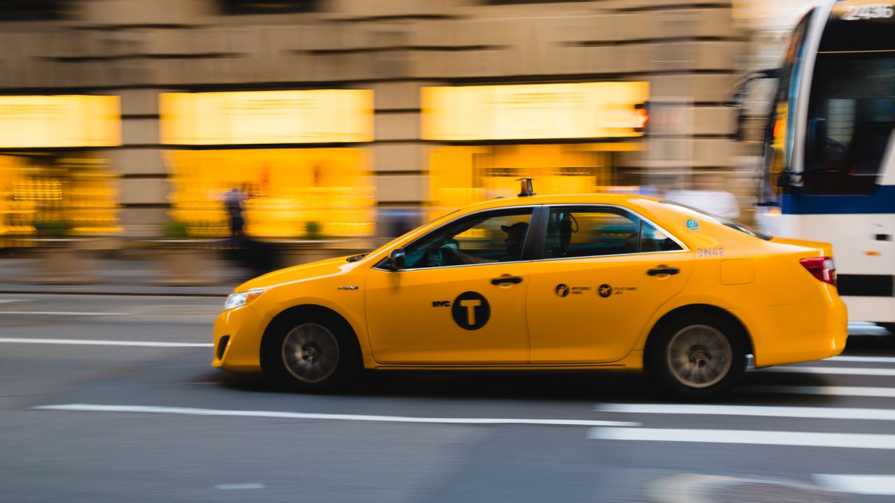 why-choose-us A New York City yellow taxi speeds through urban streets, capturing the bustle of city life.