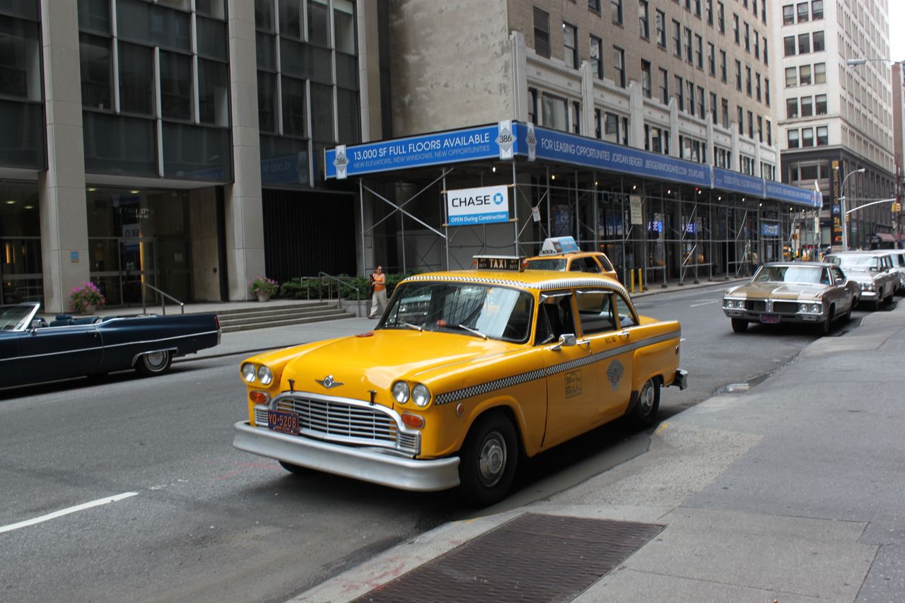 services-02 Vintage yellow taxi cab parked on a bustling New York City street.