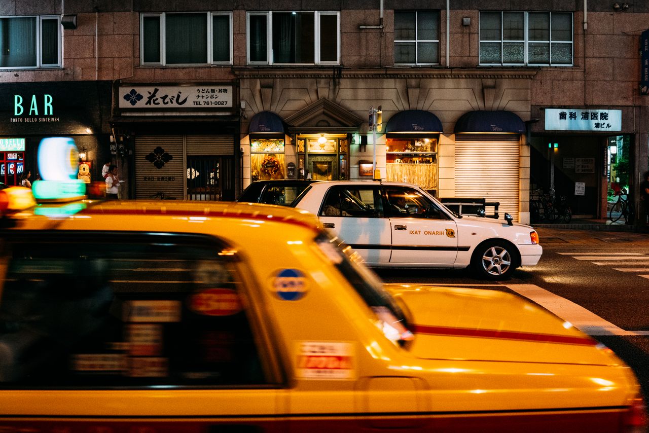 services-03 Dynamic Tokyo street scene featuring yellow taxis and illuminated storefronts at night.