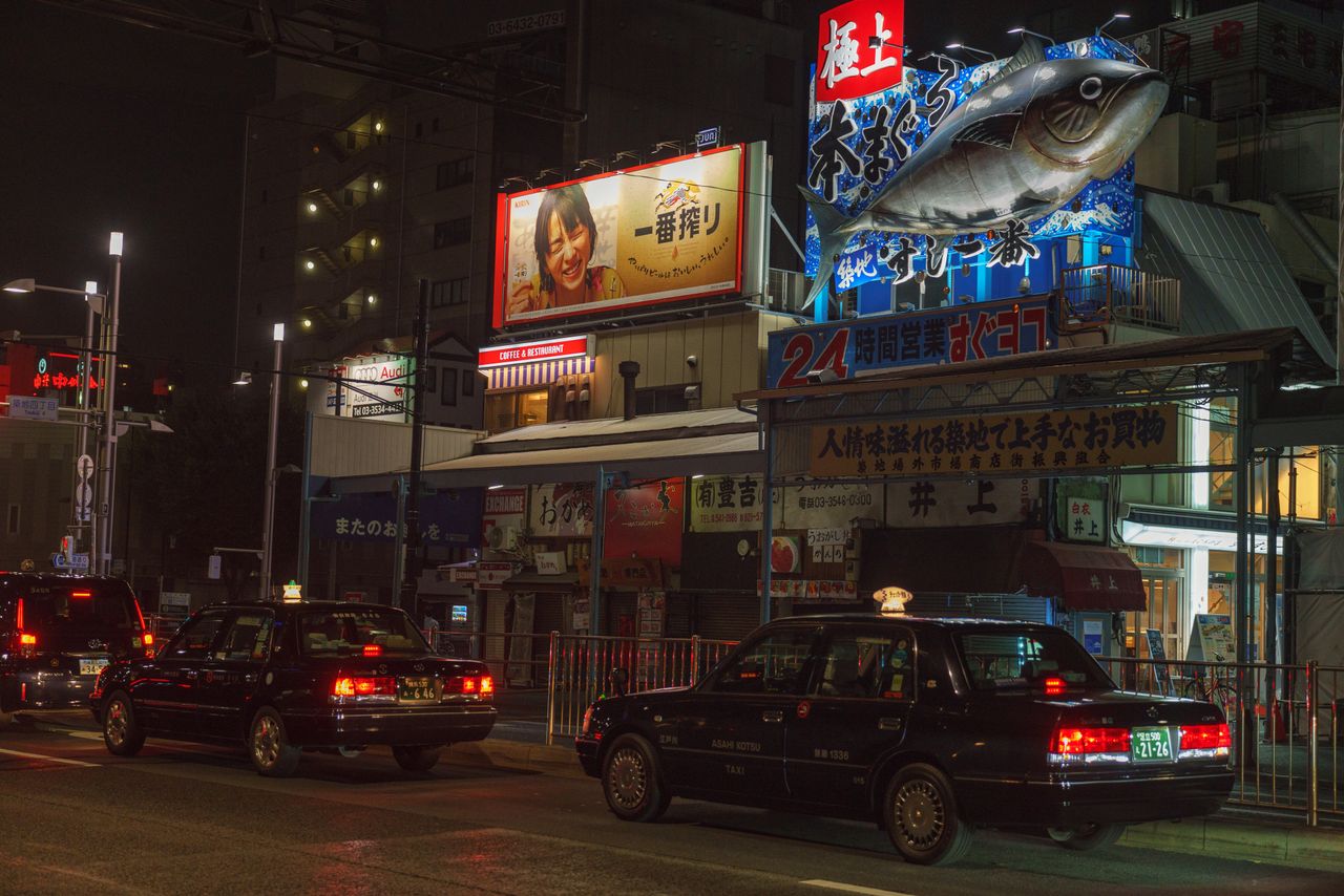 our-experience Illuminated street in Chuo City, Tokyo, featuring taxis and vibrant billboards at night.